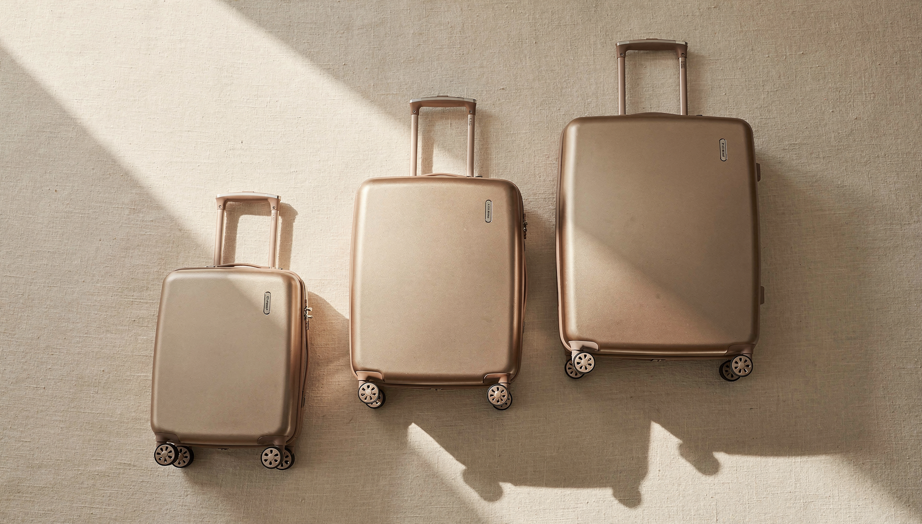 Three premium hardside spinner suitcases in champagne tones arranged by size — carry-on, medium checked, and large checked