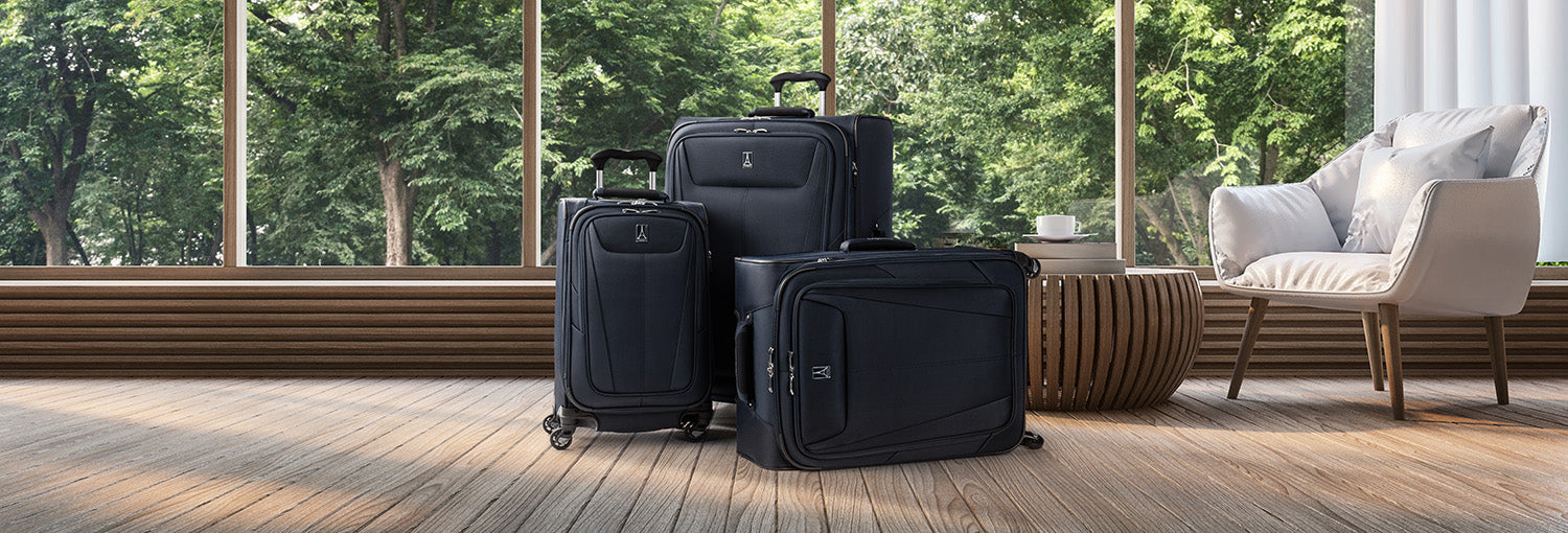 Three-piece navy blue softside luggage set in a modern interior with forest-view windows, wood flooring, and contemporary seating.