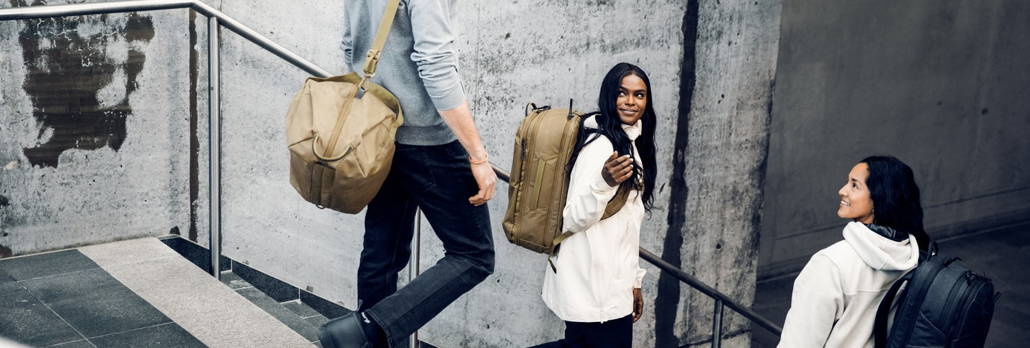 Three travelers carrying duffel bags and travel backpacks while walking through a modern urban transit space.