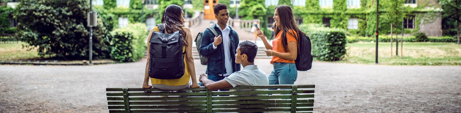 Group of students wearing everyday backpacks while socializing outdoors on a university campus.