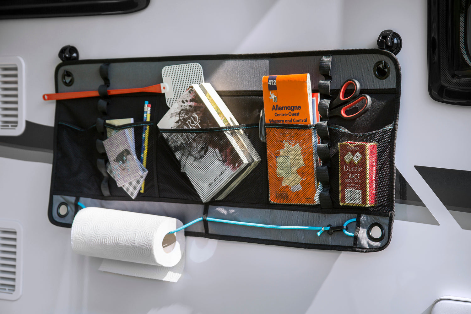 Wall-mounted travel organizer with mesh storage pockets holding maps, notebooks, tools, and camping essentials inside a camper van.