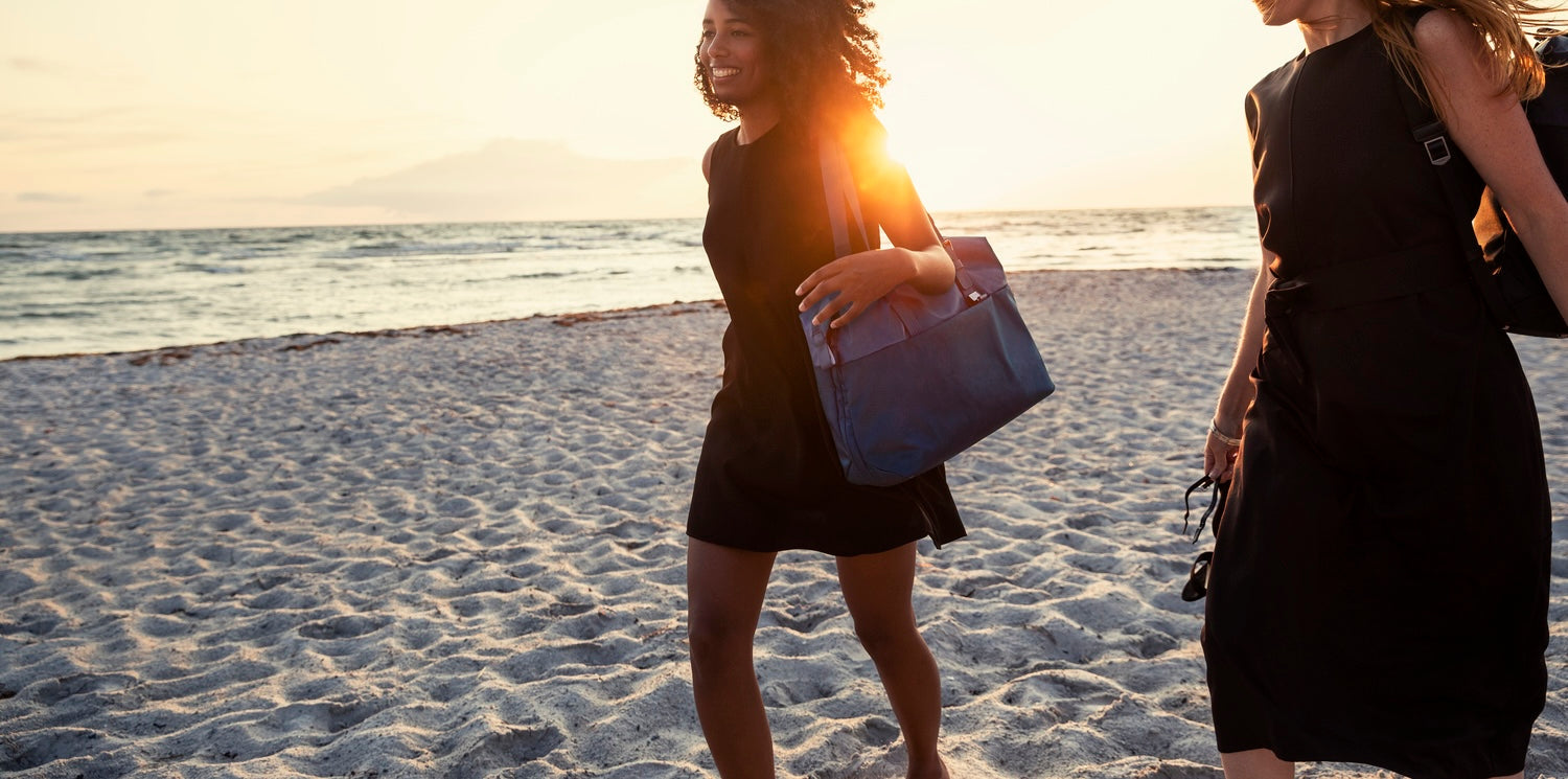 Two women walking along the beach at sunset carrying lightweight tote bags and backpacks for travel and everyday use.