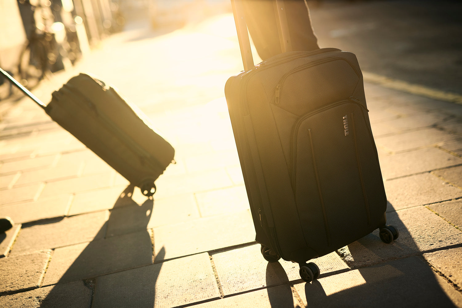 Two suitcases on wheels on a sunlit pavement