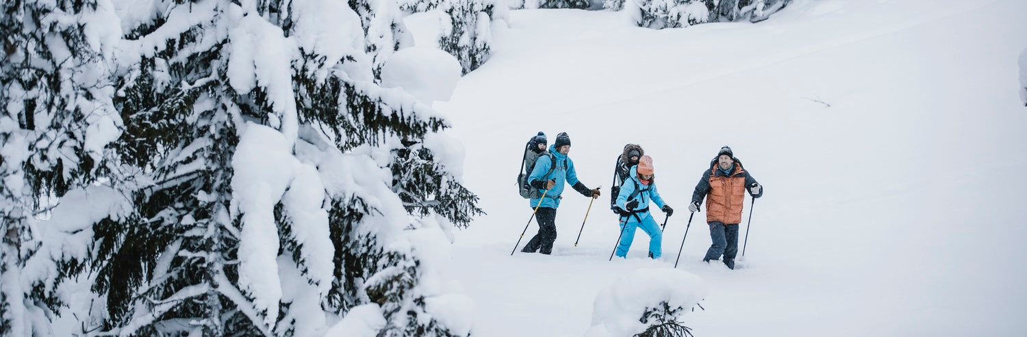 Family hiking through deep snow with winter backpacks and trekking poles in a snowy mountain landscape.
