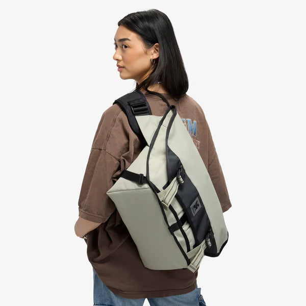 Woman wearing a sage green Chrome Citizen 15L messenger bag across her back, rear view