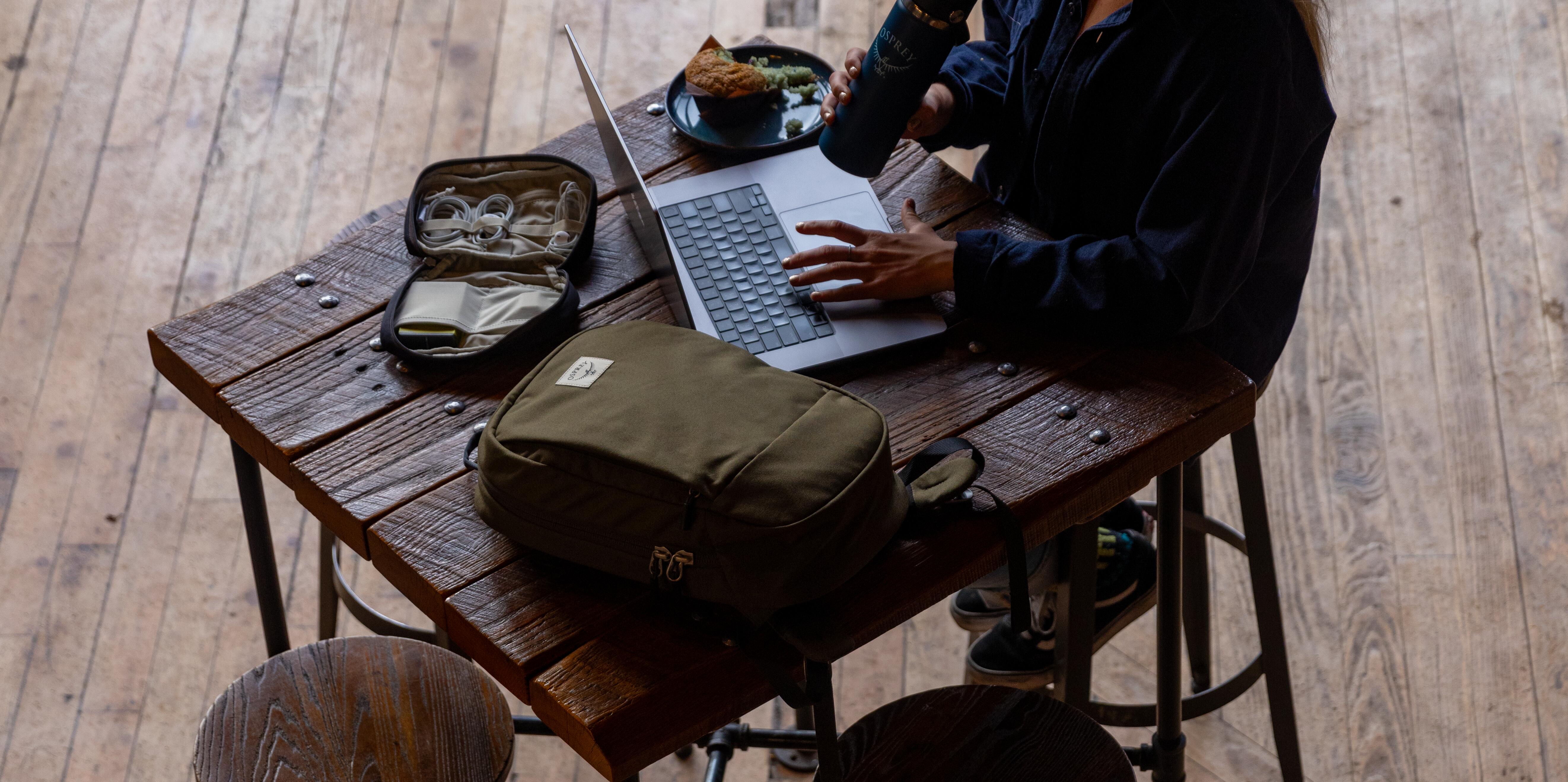 Person using a laptop at a wooden table with a bag and snacks on the table.