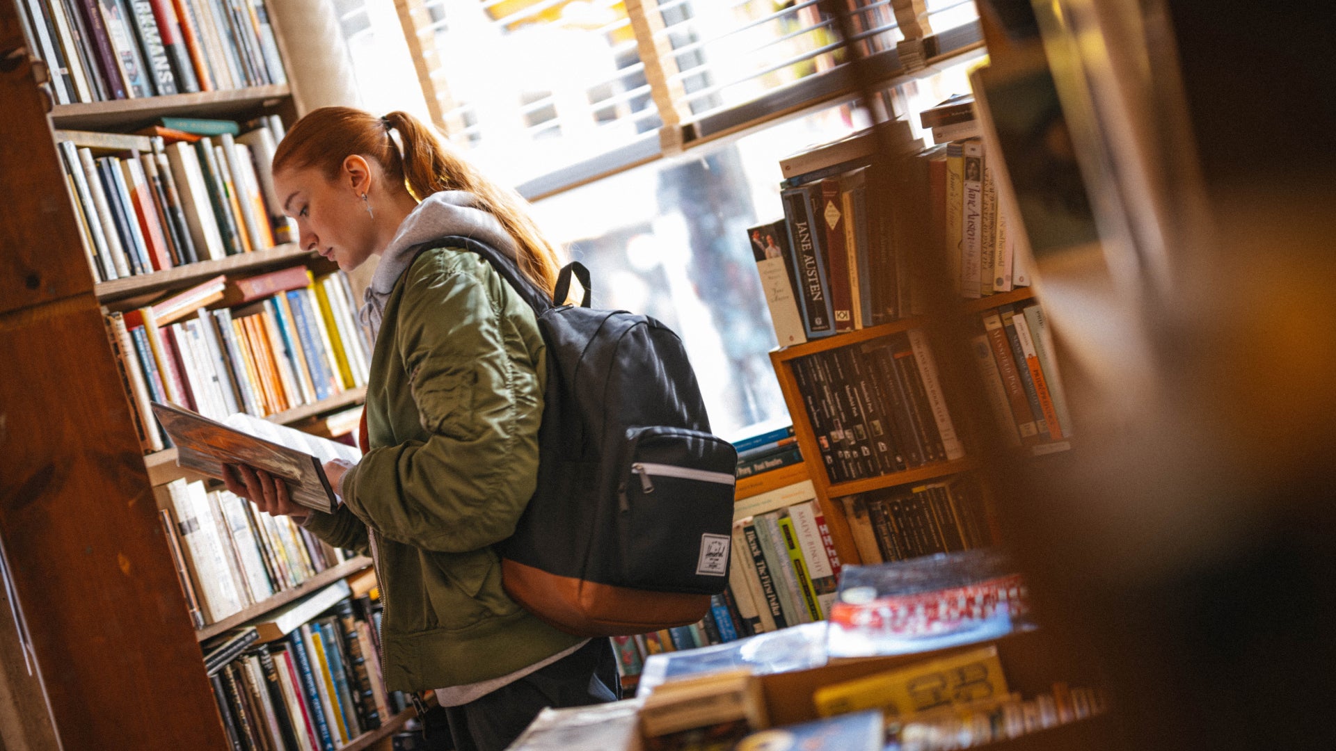 Young woman browsing books in bookstore with everyday backpack