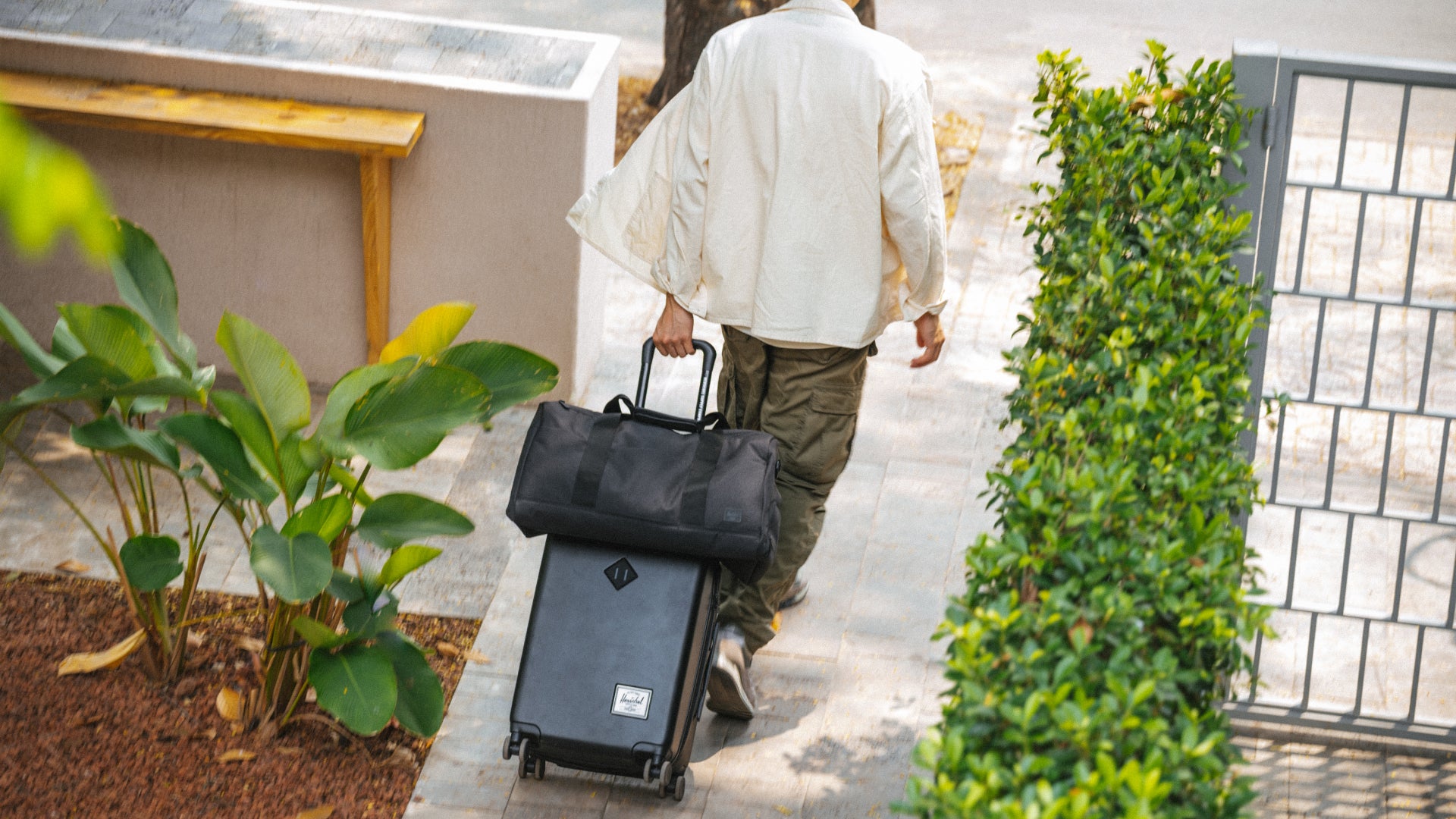 Person walking with a suitcase and duffel bag on a sidewalk