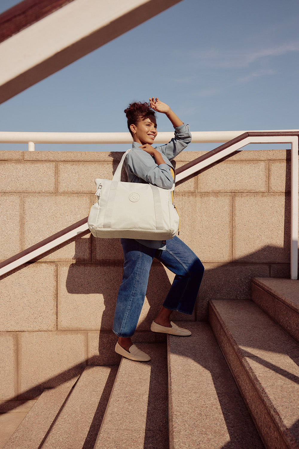 Woman with a white tote bag on a rooftop with a clear blue sky.