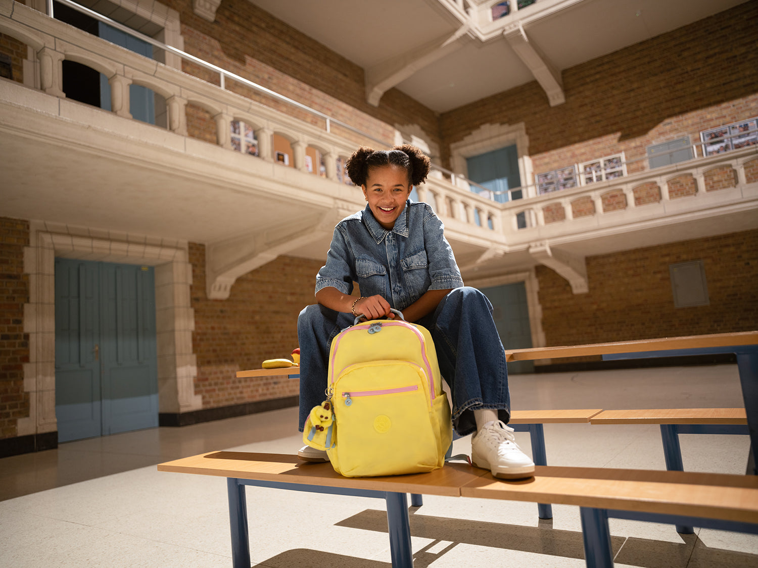 Child sitting on a bench in a school hallway with a yellow backpack