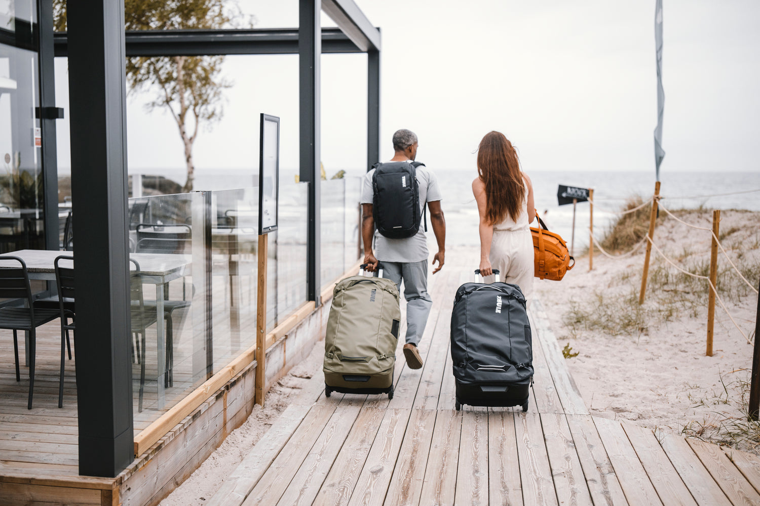 Two people with luggage walking towards a beach.