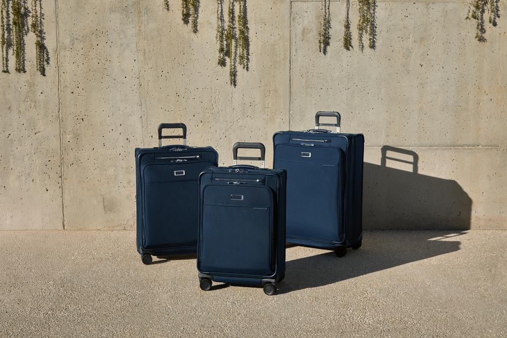 Three navy blue suitcases of different sizes against a concrete wall.